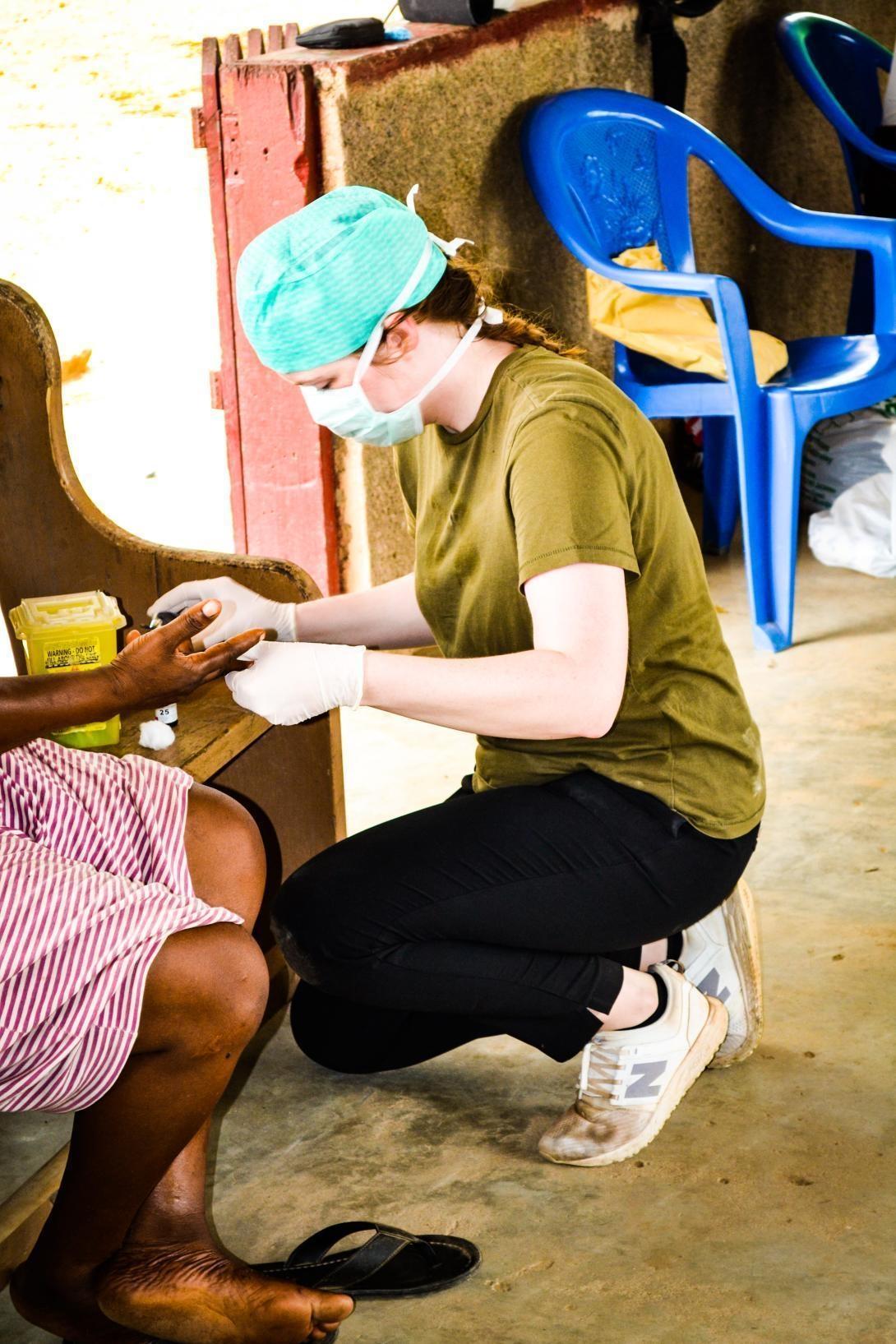A healthcare volunteer in wearing a protective mask and gloves treats a patient on a medical internship in Ghana